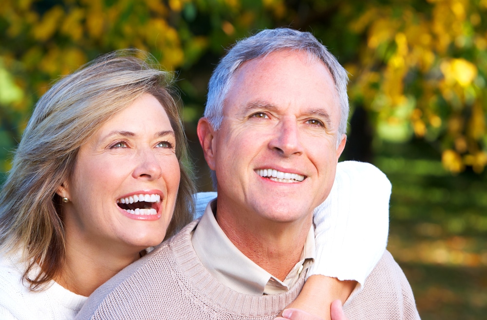 Two happy seniors smiling broadly, showcasing healthy teeth, symbolizing the benefits of understanding Medicare dental coverage.