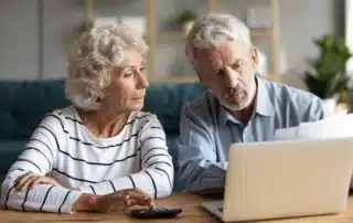 Senior couple reviewing documents and using a laptop to explore their Medicare options during the annual enrollment period.