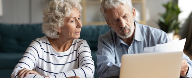 Senior couple reviewing documents and using a laptop to explore their Medicare options during the annual enrollment period.